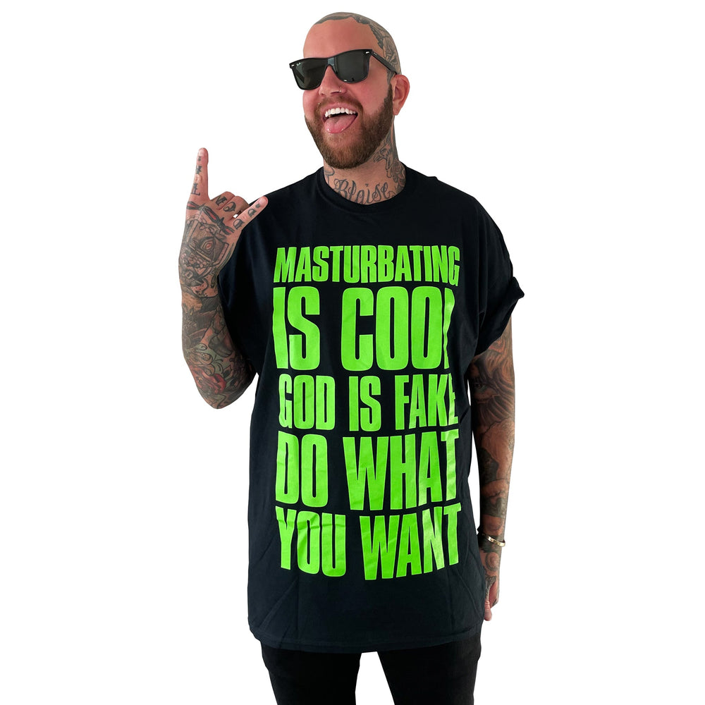 A tattooed man in sunglasses smiles, making a rock on gesture while wearing a bold Stay Sick Clothing t-shirt with neon green MASTURBATING IS COOL. GOD IS FAKE. DO WHAT YOU WANT. text, showing off his God Is Fake tee style.