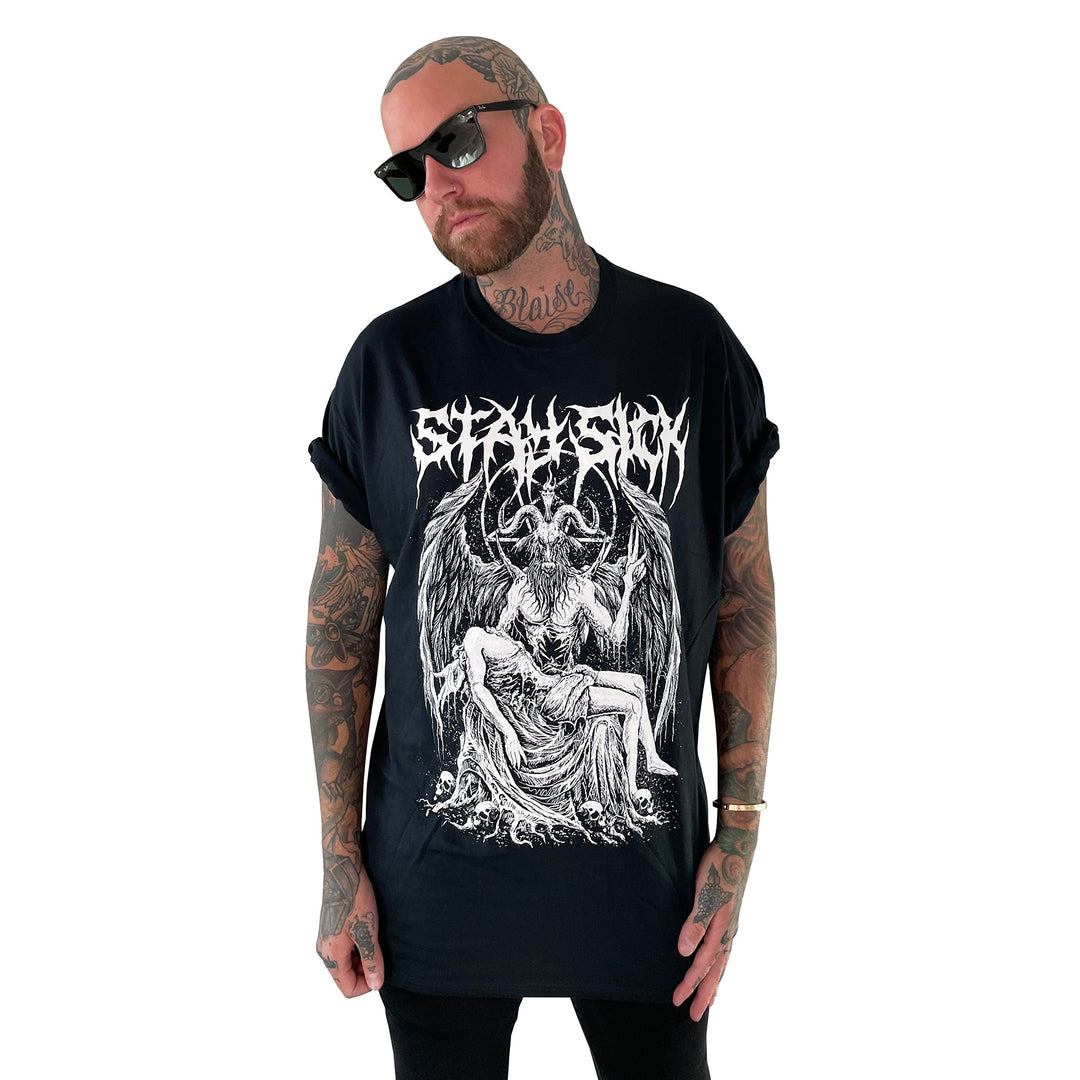 A tattooed person with a beard and sunglasses wears a black Stay Sick Clothing Baphomet T-shirt, featuring a gothic illustration of a winged demon, a reclining figure, and an intricate band logo above the graphic.