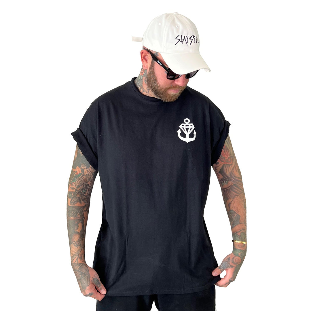A man with tattoos wears sunglasses, a white cap with black text, and a Stay Sick Clothing Black T-Shirt featuring a white anchor emblem on the chest, standing against a white background.