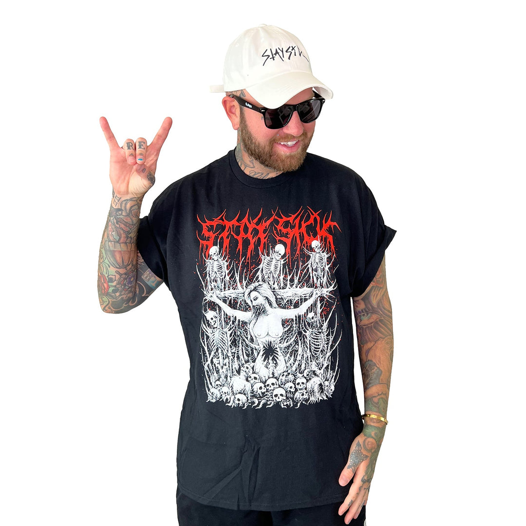 A bearded man with tattoos wears sunglasses, a white cap, and a black Stay Sick Clothing T-shirt with bold red and white artwork. He smiles and flashes the rock on hand sign against a white background.