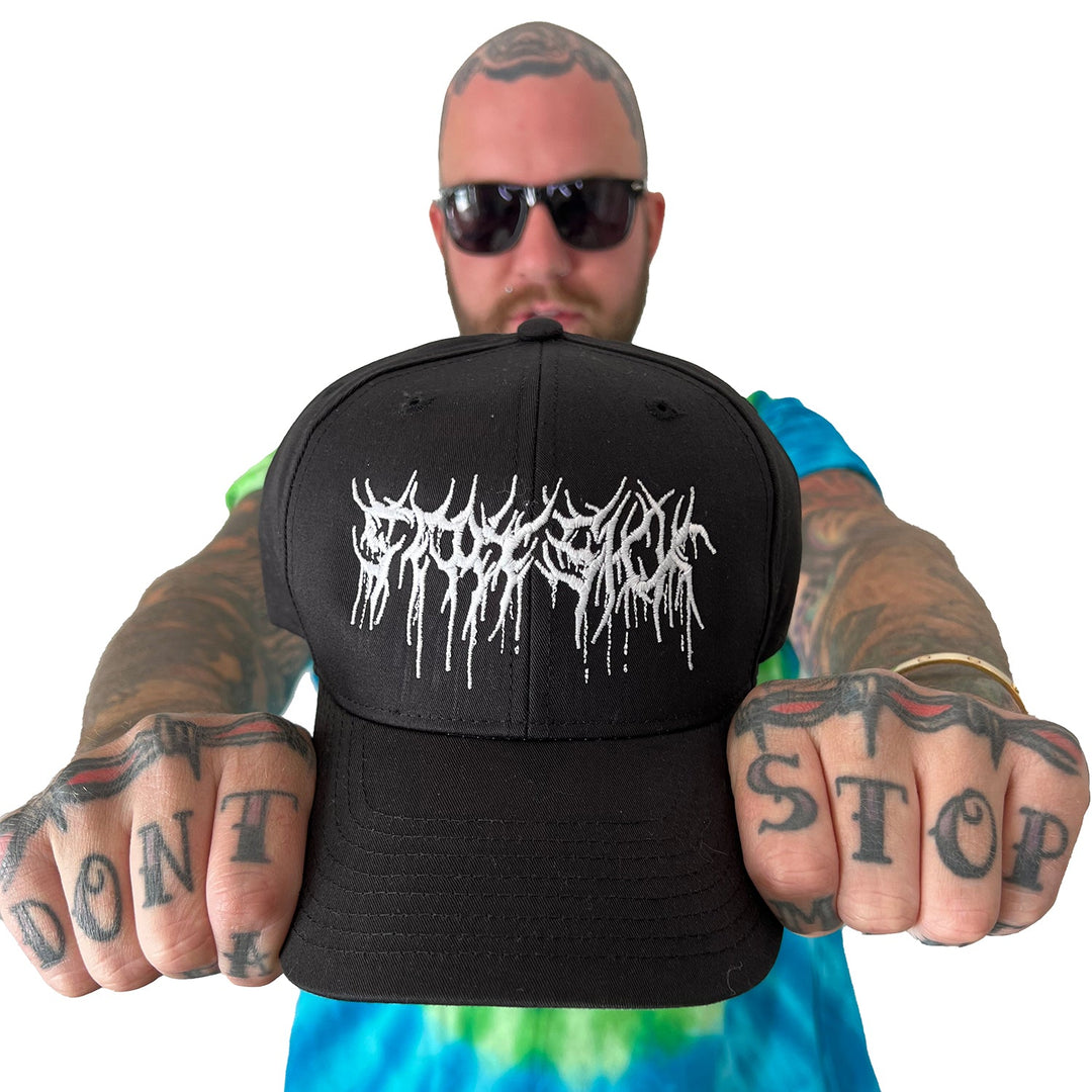 A tattooed man in sunglasses and a tie-dye shirt holds a black Stay Sick Clothing cap with white, drippy lettering (Medium Large Fit) toward the camera; his knuckles say DONT STOP against a white background.