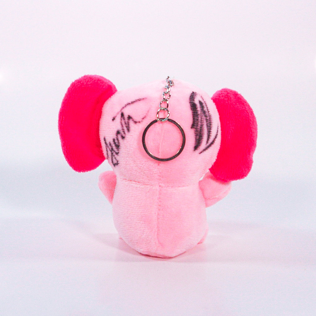 A small pink plush elephant keychain from Pink Elefants, with large pink ears, seen from the back and featuring black markings or signatures on its head.