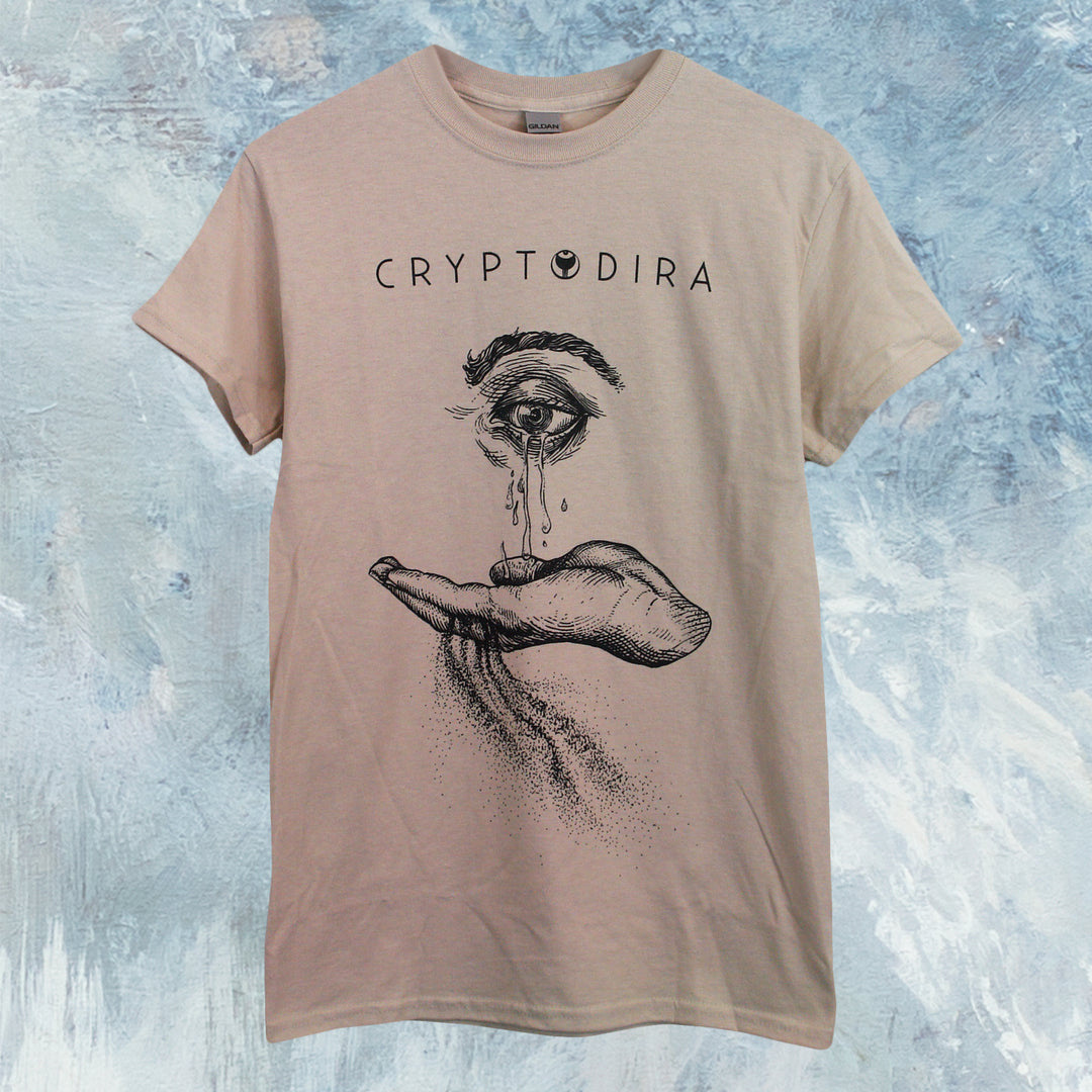 A classic fit Cryptodira beige tee features ‘CRYPTODIRA’ above a teary eye and open hand with textured shading. Made from a soft cotton-poly blend, the shirt appears atop a blue and white textured background.