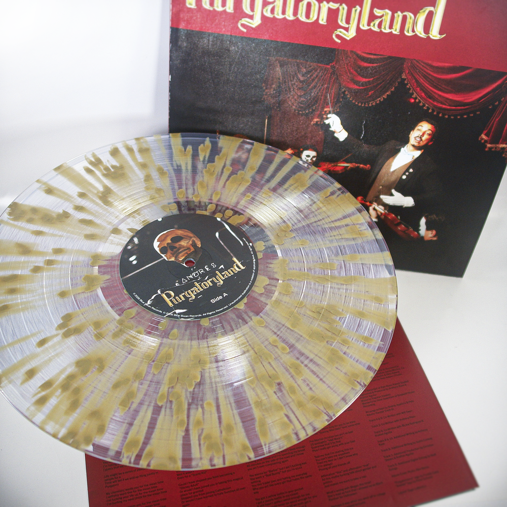 A translucent limited edition Andrés vinyl with gold splatter design rests on a red sheet with text, in front of the Purgatoryland album cover featuring a theatrical performer.