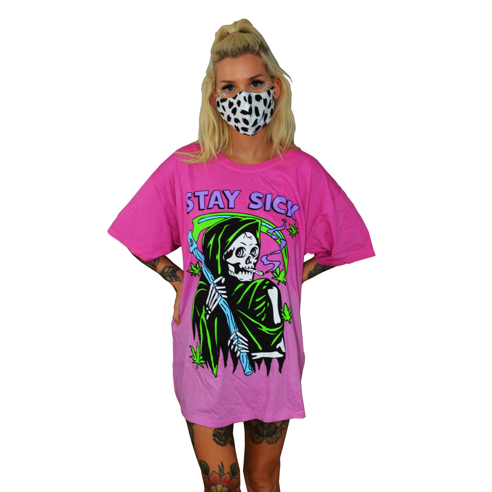 A woman wears a black-and-white spotted mask and a loose pink ombre Stay Sick Clothing T-shirt with a neon Grim Reefer, cannabis leaves, and STAY SICK text. The background is plain white.