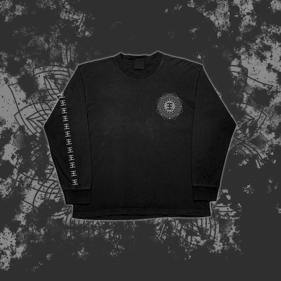 A black Reflections long sleeve shirt featuring a printed geometric mandala on the left chest and repeated white geometric symbols down the right sleeve, shown against a dark, grungy patterned background.