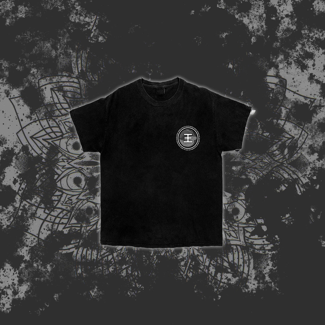 A black Reflections t-shirt with a white circular emblem on the left chest is centered on a dark, splattered background featuring a faint decorative mandala pattern.