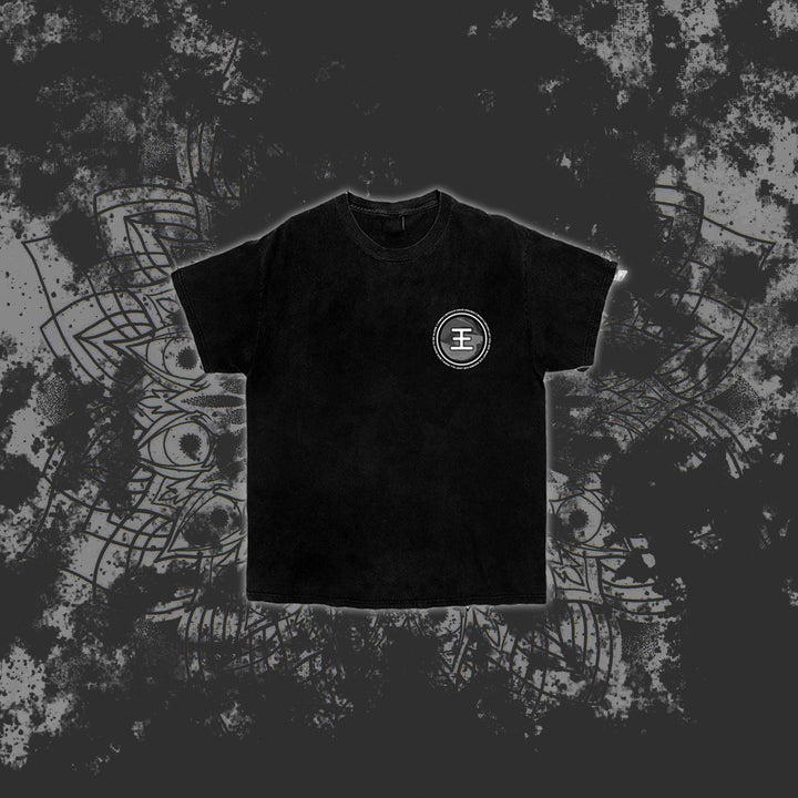 A black Reflections t-shirt with a white circular emblem on the left chest is centered on a dark, splattered background featuring a faint decorative mandala pattern.