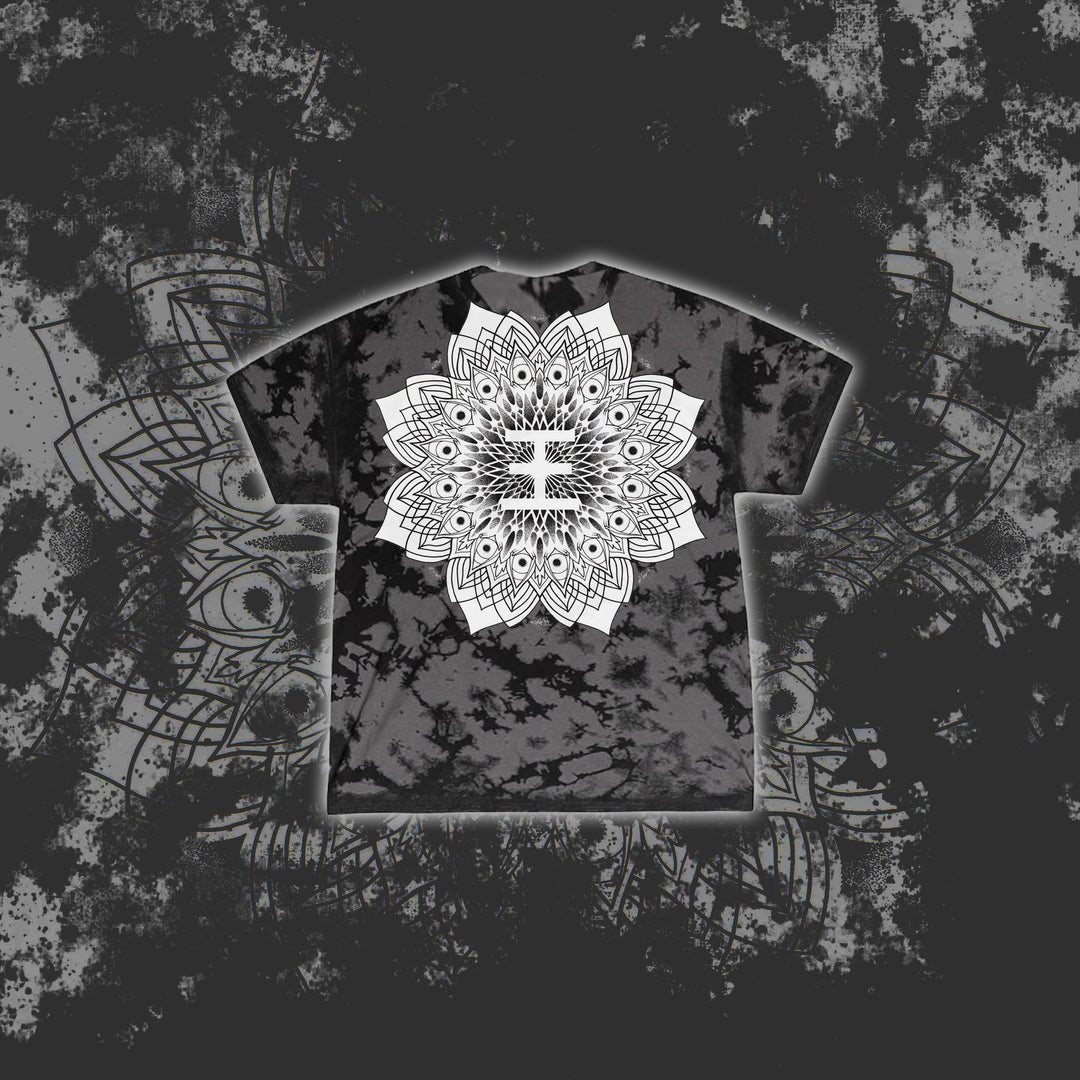 A black and gray tie-dye Reflections T-shirt features a bold white mandala design centered on the chest, set against a matching mandala and splatter background—ideal for fans of printed tees.