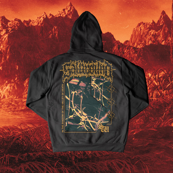 A black Saltwound pullover hoodie featuring abstract gold and white graphics, band logo, and “In the Shadow of the Valley of Death” text on the back, classic fit, shown against a surreal red-orange mountainous backdrop.