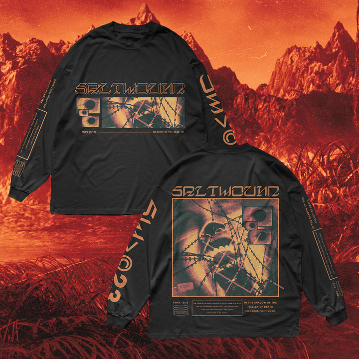 Two black Saltwound long-sleeve shirts with orange graphics and abstract designs are shown front and back on a surreal red-orange mountain background. The 100% cotton shirts display text, barbed wire, and geometric patterns.