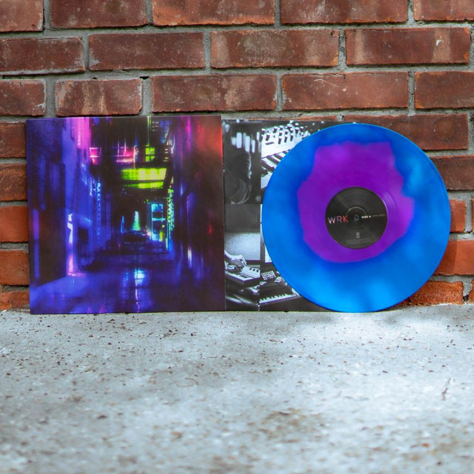A blue and purple marbled Opaque Neon Magenta Vinyl of William Ryan Key’s Everything Except Desire, partially out of its sleeve with neon city art, stands against a red brick wall.