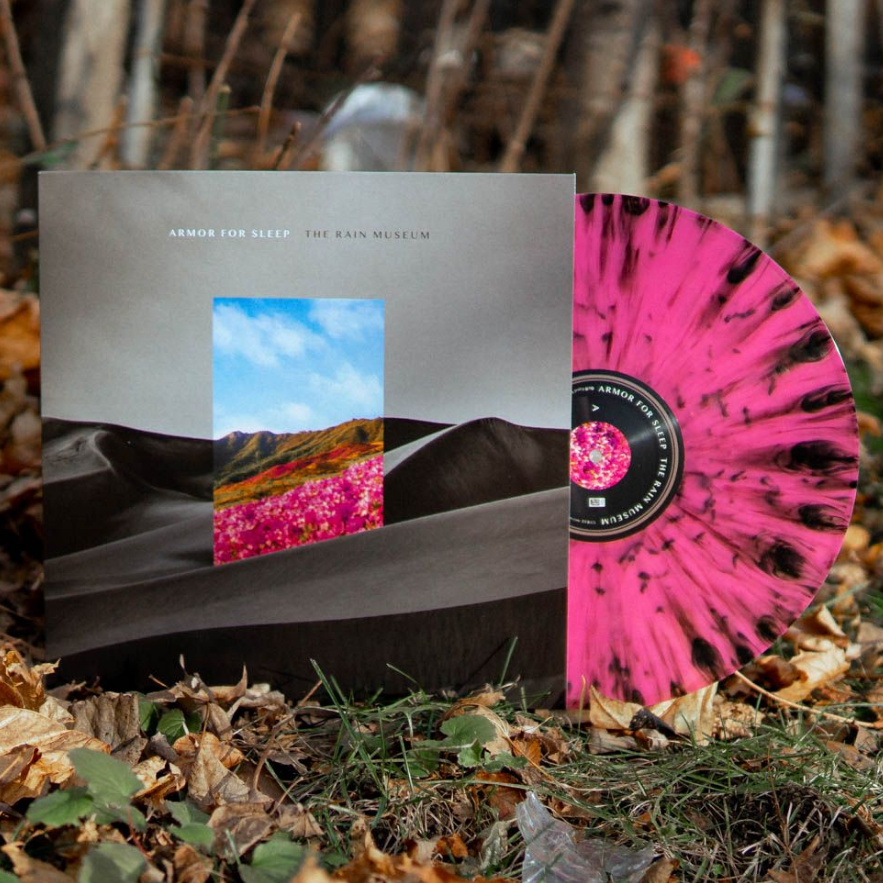 A pink-and-black splattered Armor For Sleep vinyl rests against its album cover, which shows a black-and-white landscape with a colorful field and blue sky cutout, surrounded by fallen leaves and branches.