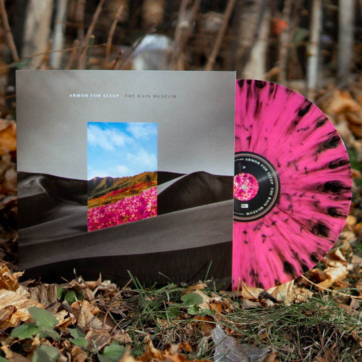 A pink-and-black splattered Armor For Sleep vinyl rests against its album cover, which shows a black-and-white landscape with a colorful field and blue sky cutout, surrounded by fallen leaves and branches.