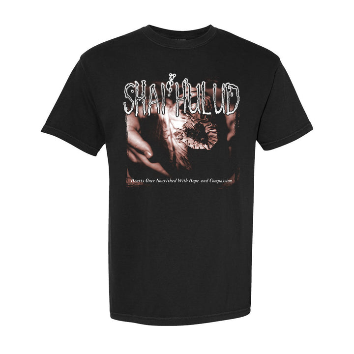 A black Shai Hulud T-shirt with stylized white SHAI HULUD text above a sepia image of hands, and “Hearts Once Nourished With Hope and Compassion.” printed below.