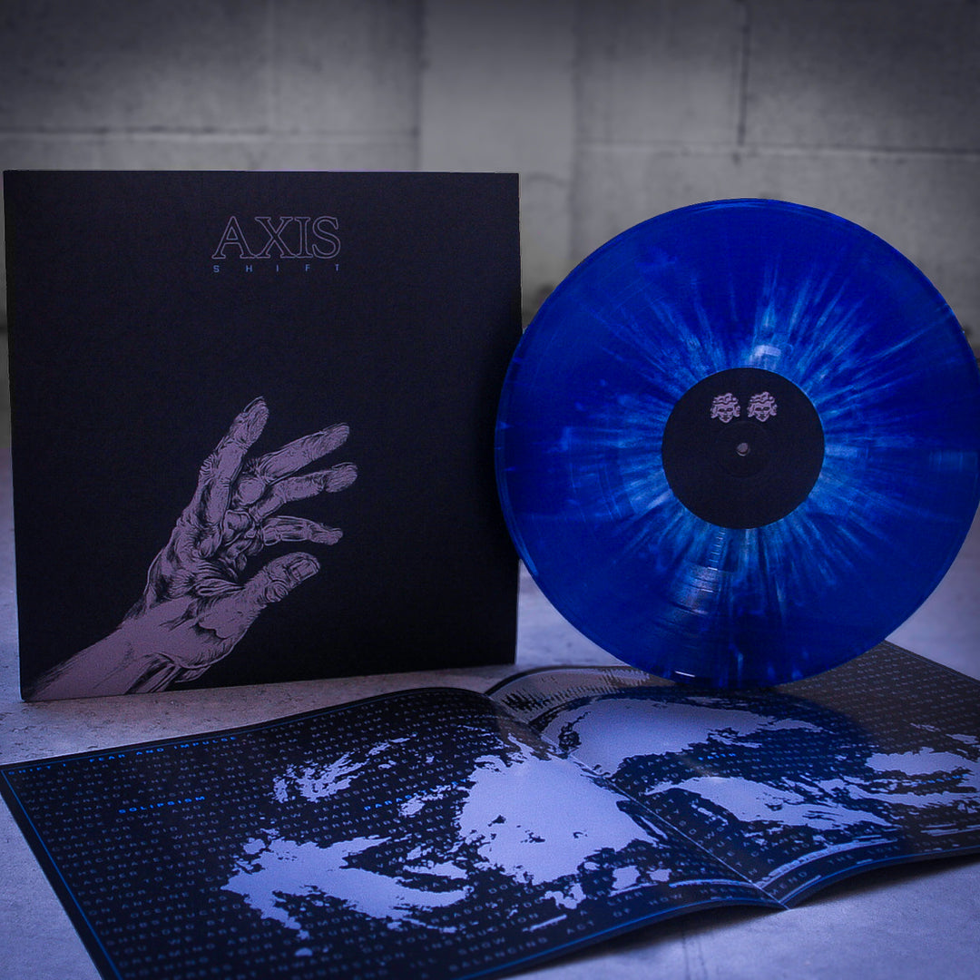 A blue, translucent Axis vinyl record titled "Shift" stands upright beside its black album cover with an illustrated hand. An open booklet with black-and-white artwork lies in front on a gray surface.