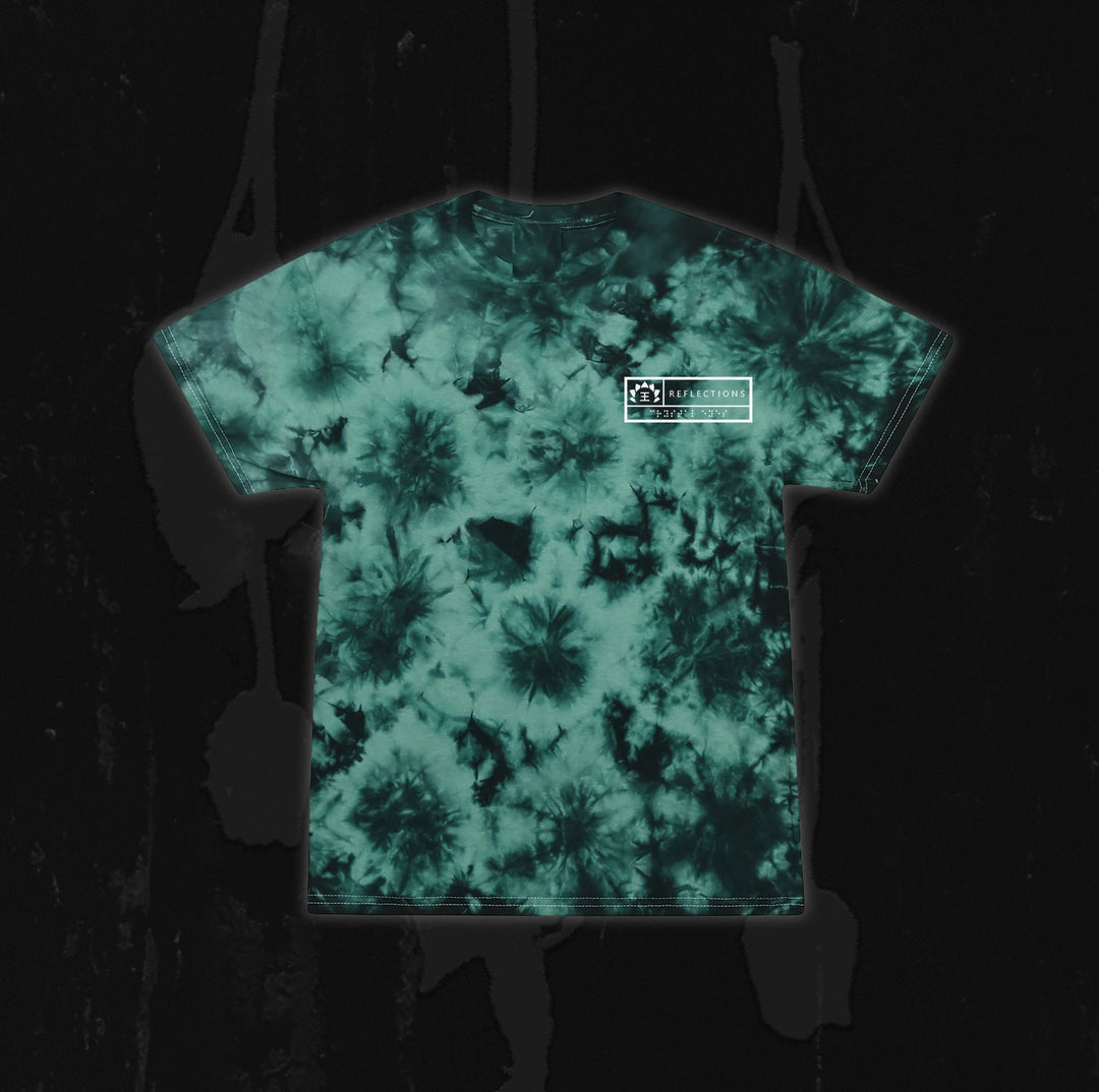 A green and black tie-dye t-shirt from Reflections, featuring a small white rectangular Crystal Eyes logo on the upper left chest, displayed on a dark, textured background.