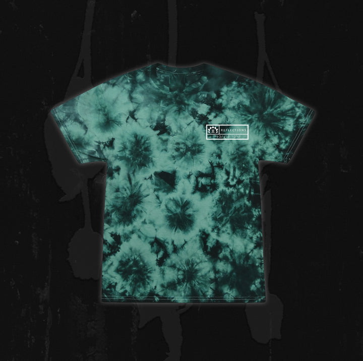 A green and black tie-dye t-shirt from Reflections, featuring a small white rectangular Crystal Eyes logo on the upper left chest, displayed on a dark, textured background.