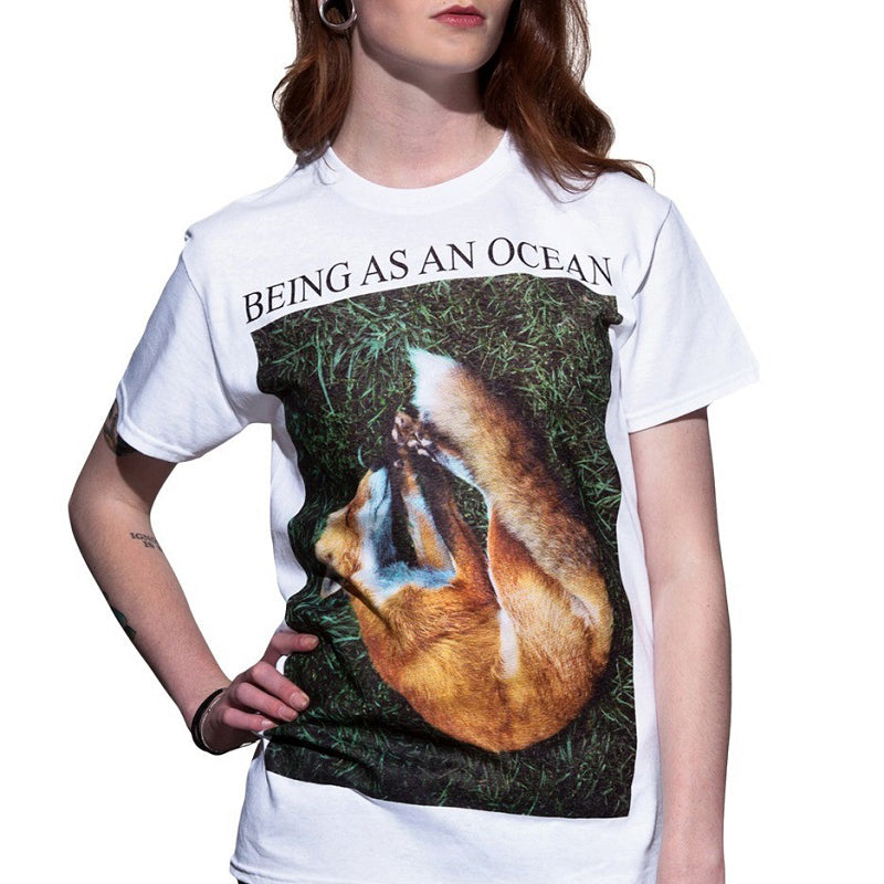 image of a woman from the neck down with her hand on her hip wearing a white tee shirt on a white background. tee has full body print that says in black on top, being as an ocean with a photo of a sleeping fox on green grass.