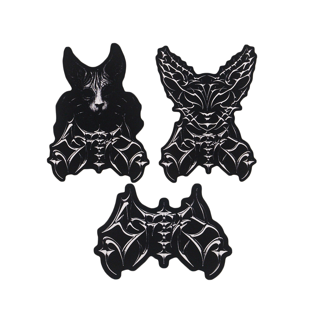 Three black-and-white stickers: two stylized bat heads with intricate patterns at the top, and one abstract bat body with wings and detailed linework at the bottom, all set against a white background.