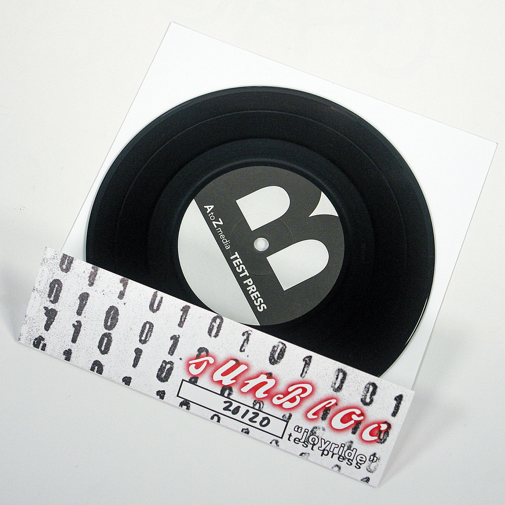 A black vinyl record in a white sleeve labeled “AztecZero TEST PRESS” is shown. In front, a patterned strip reads “SUNBLOC” (the brand) and “20120,” channeling hardcore and alternative music energy.