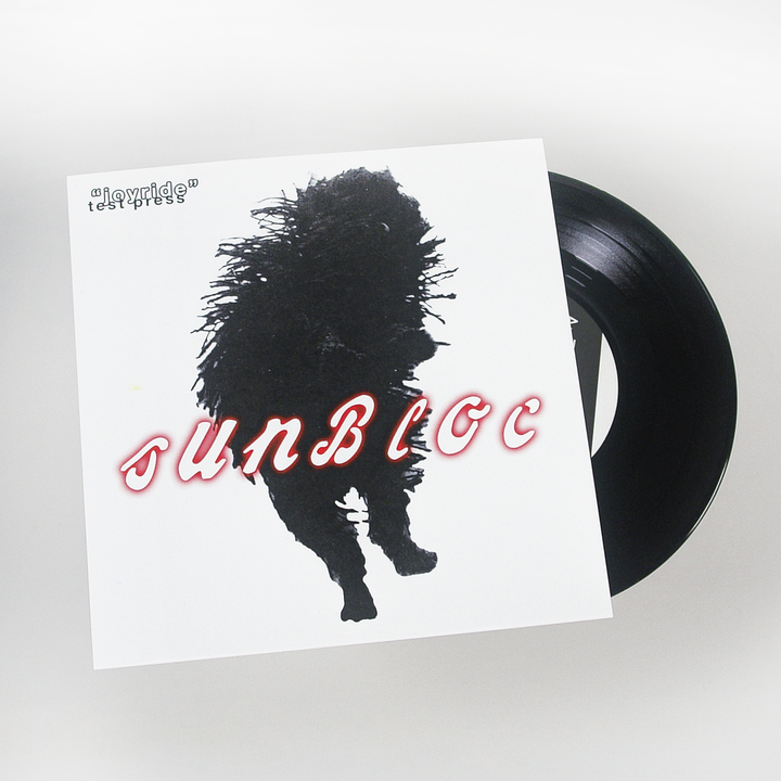 A vinyl record halfway out of its sleeve, displaying the Sunbloc brand name in bold stylized letters above a black silhouette of a running animal. "Joyride test press" appears in small text at the sleeve's top left, suggesting alternative music.