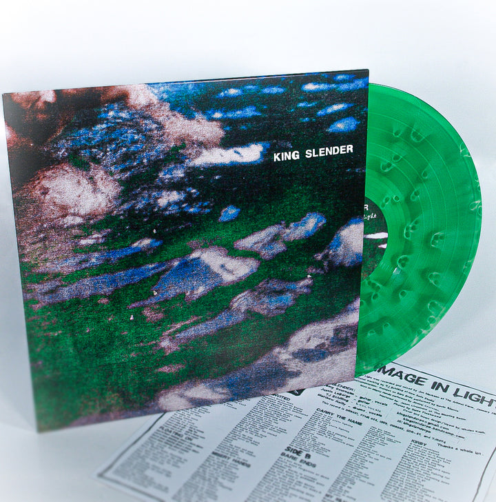 A green 12" vinyl record by King Slender partially slides from its vibrant, abstract album cover, with a black-text lyric sheet nearby on a white surface—echoing an emotional hardcore vibe.