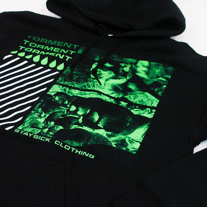 Black hoodie by Stay Sick Clothing featuring green graphic frogs, TORMENT repeated three times, diagonal white stripes, green droplets, and STAYSICK CLOTHING text—capturing the intriguing essence of Torment Black.