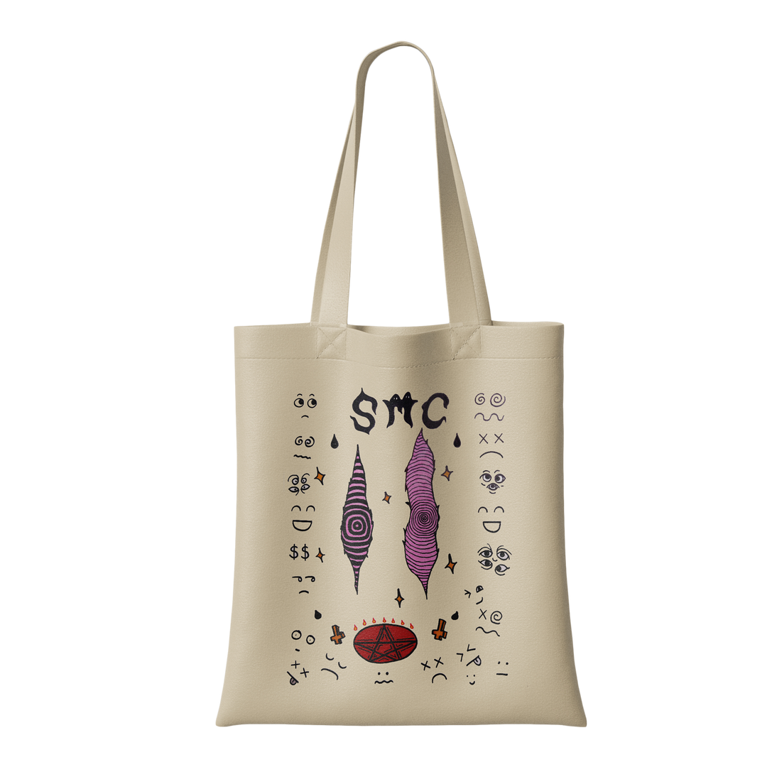 Strawberry Milk Cult’s eco-friendly Natural Tote Bag features two purple, abstract, cone-shaped faces, “SMC” at the top, a red oval at the bottom, and scattered small black doodles and symbols.