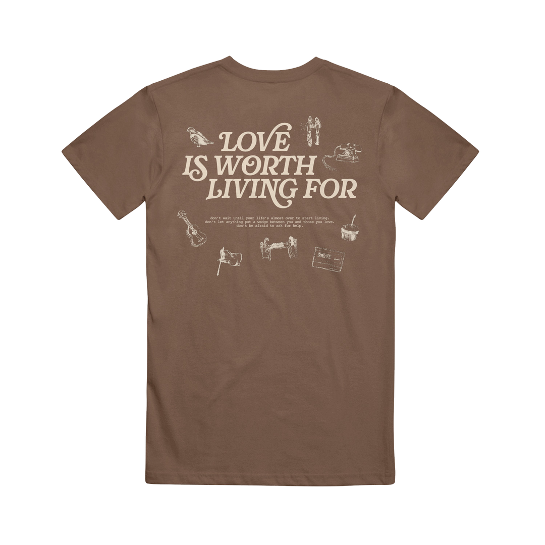 Joshua Bassett Brown Espresso Tee features "Love Is Worth Living For" in bold white text on the back, accented by small white guitar, camera, and cassette tape illustrations.
