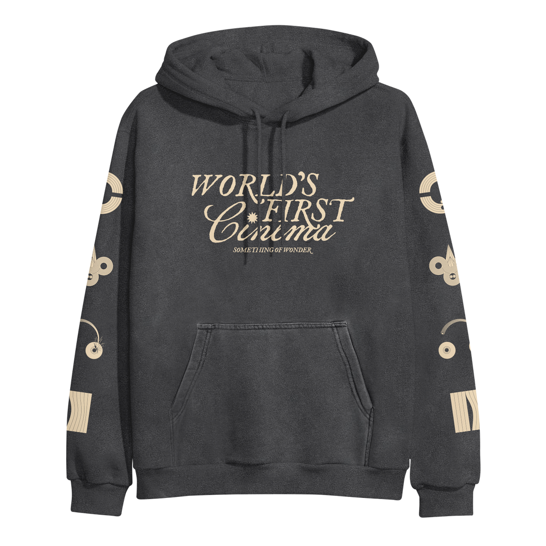 A dark gray World's First Cinema pullover hoodie with cream text "WORLDS FIRST CINEMA SOMETHING OF WONDER" on the front, abstract cream graphics on both sleeves, a front pocket, and drawstrings. Midweight by Independent Trading Company.