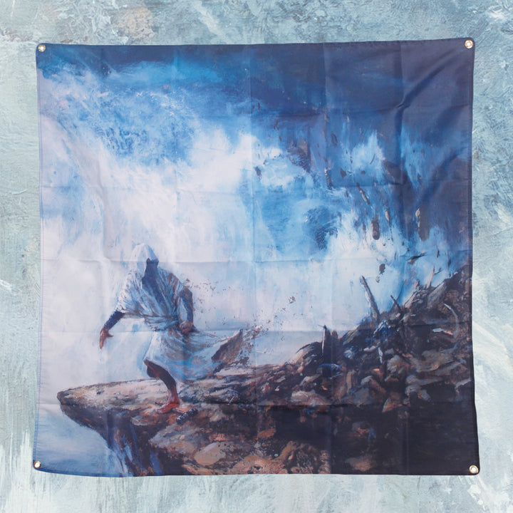 A hooded figure stands on a rocky cliff before a swirling blue and white storm, debris scattered and misty air behind—an epic scene printed on a Cryptodira 4' x 4" wall flag with sturdy grommets.