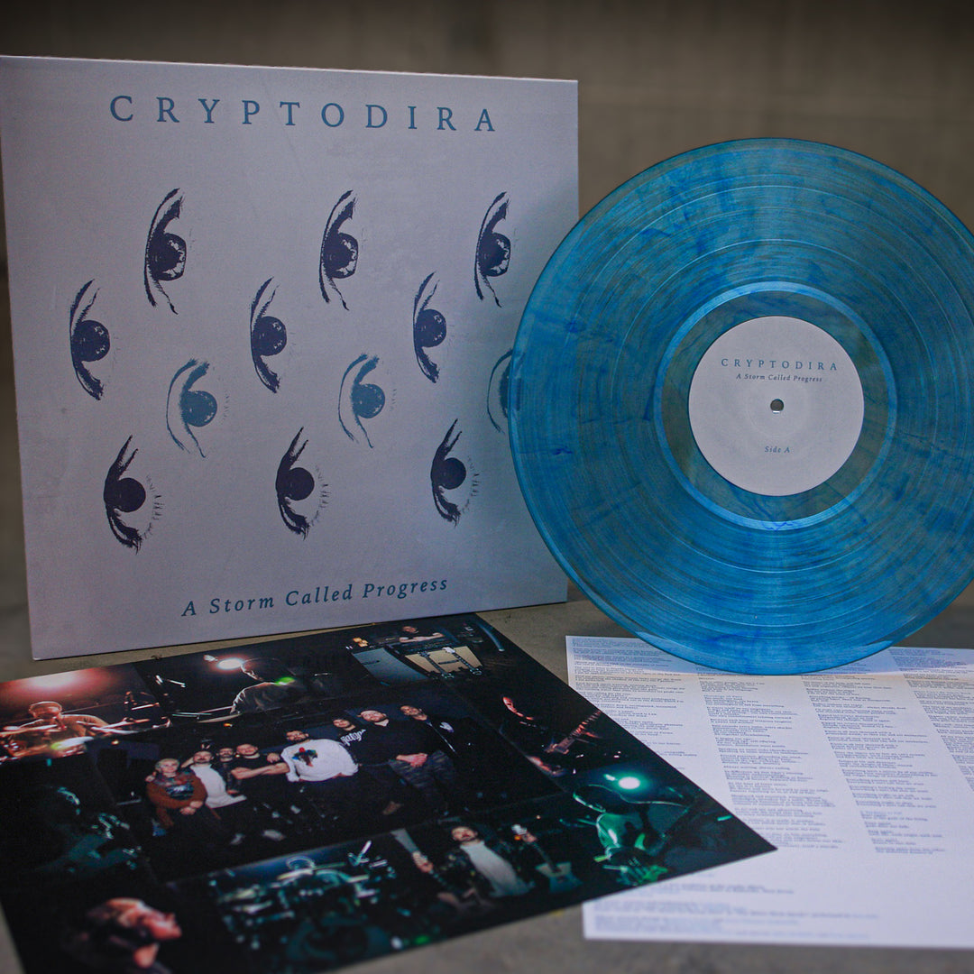 A limited edition Cryptodira vinyl of A Storm Called Progress is shown with its album cover, band photo insert, and lyrics sheet on a gray surface—the perfect complement to The Angel of History vinyl.