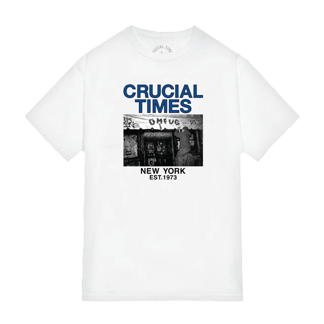 Crucial Times white Comfort Colors T-shirt features bold blue CRUCIAL TIMES text over a black-and-white street scene, with NEW YORK EST.1973 below. Available for presale now; ships 1/1/26.