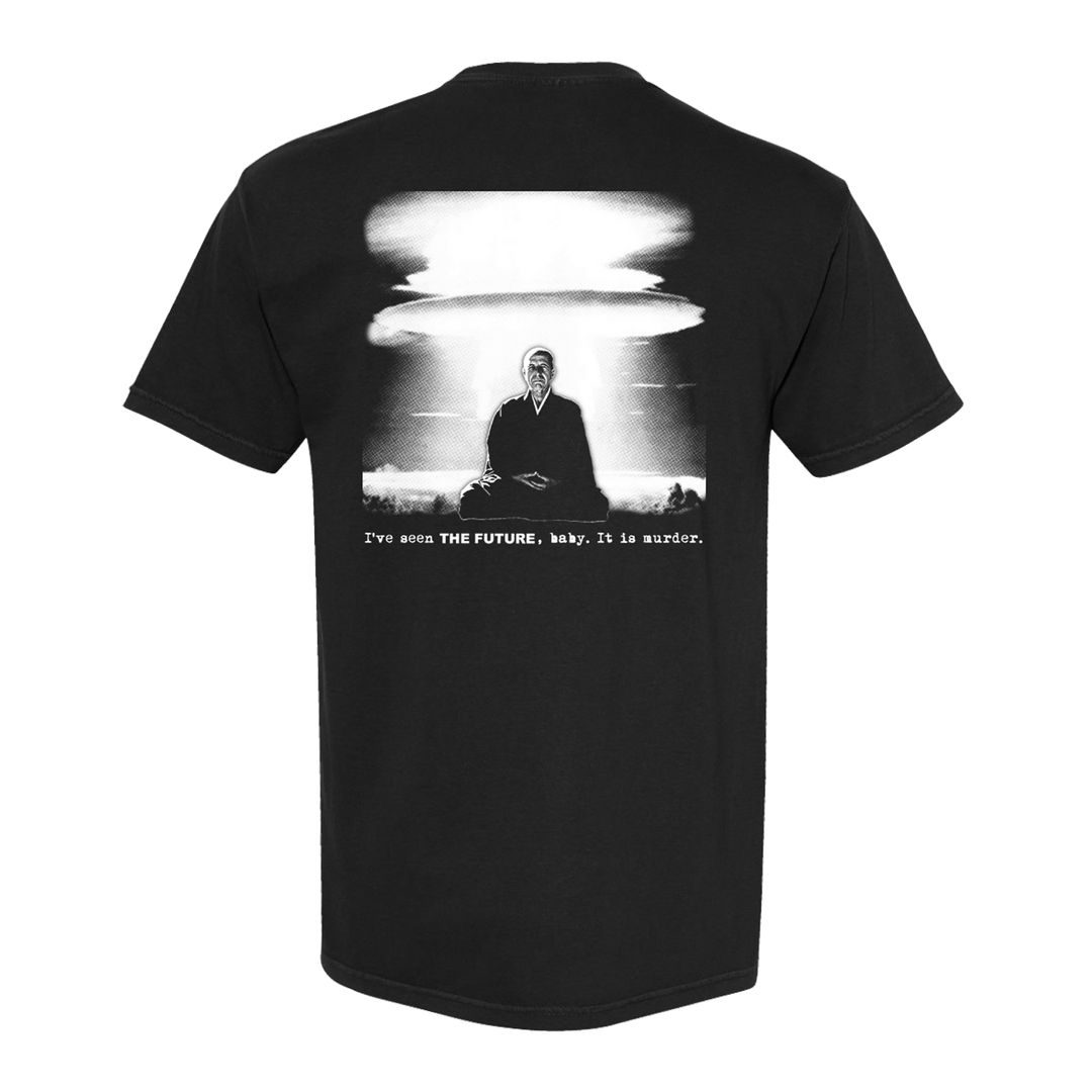 Die Young black Comfort Colors tee with a graphic of a suited man before a mushroom cloud. Below, white text reads: I’ve seen THE FUTURE, baby. It is murder.