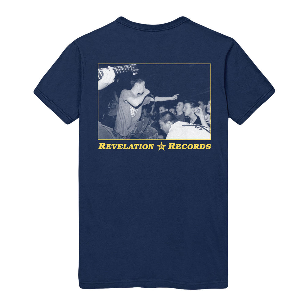 A navy blue Gildan heavy cotton t-shirt by Bold features a black-and-white photo of a band performing live, the singer leaning toward the crowd. Yellow text below reads REVELATION ★ RECORDS. Ships 9/3/25.