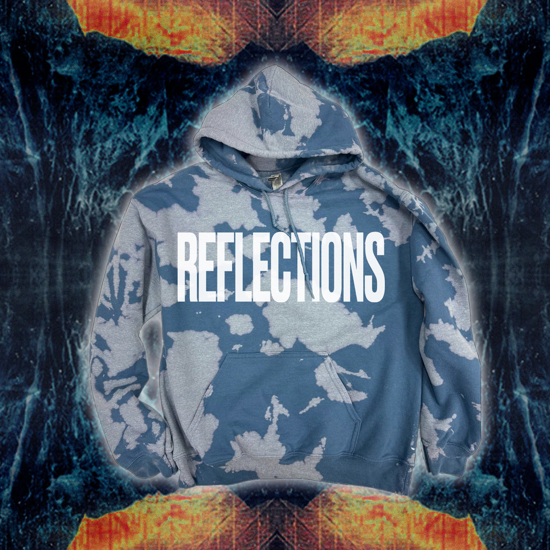 A blue and gray bleach wash hooded sweatshirt by Reflections features REFLECTIONS in bold white letters centered on the chest, set against a symmetrical abstract background with fiery orange and blue textures.