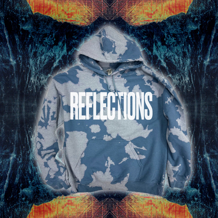 A blue and gray bleach wash hooded sweatshirt by Reflections features REFLECTIONS in bold white letters centered on the chest, set against a symmetrical abstract background with fiery orange and blue textures.