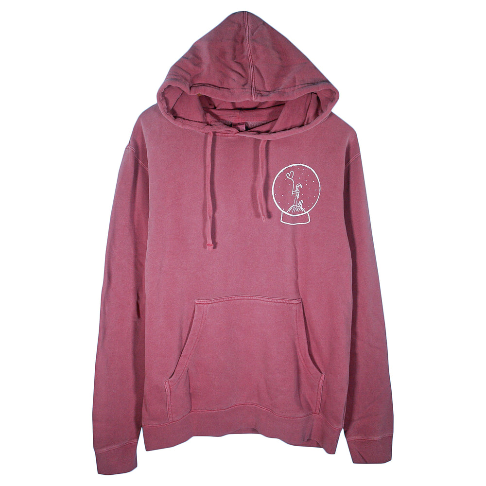 A maroon Matt Nathanson pigment-dyed pullover hoodie with a front pocket and drawstrings, featuring a small white peace sign hand in a snow globe graphic on the left chest.