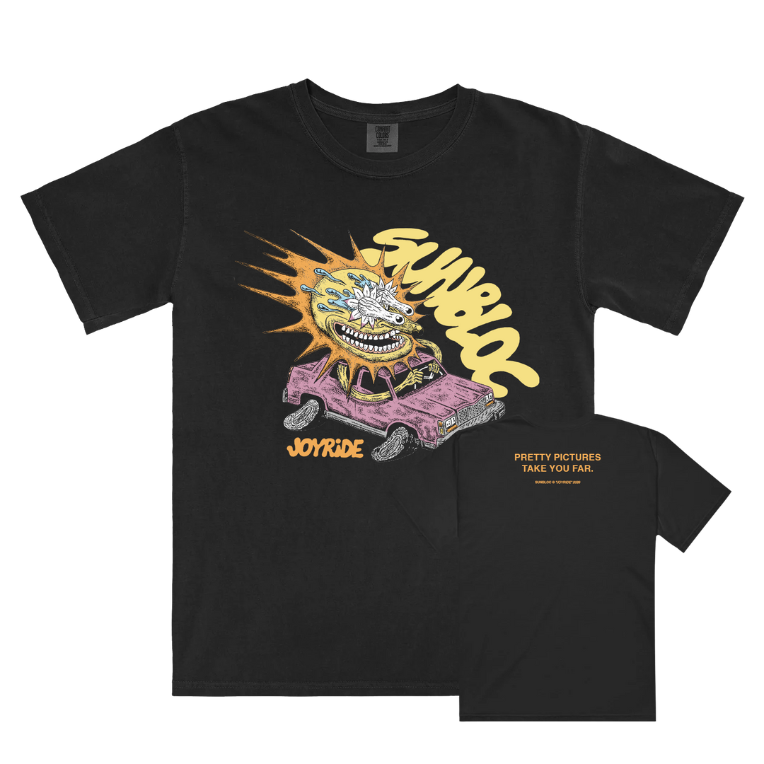 Black Comfort Colors Sunbloc shirt with a cartoon character crashing through a pink car and "SAVWLOG" and "JOY RIDE" on the front, plus bold yellow "PRETTY PICTURES TAKE YOU FAR" text on the back.