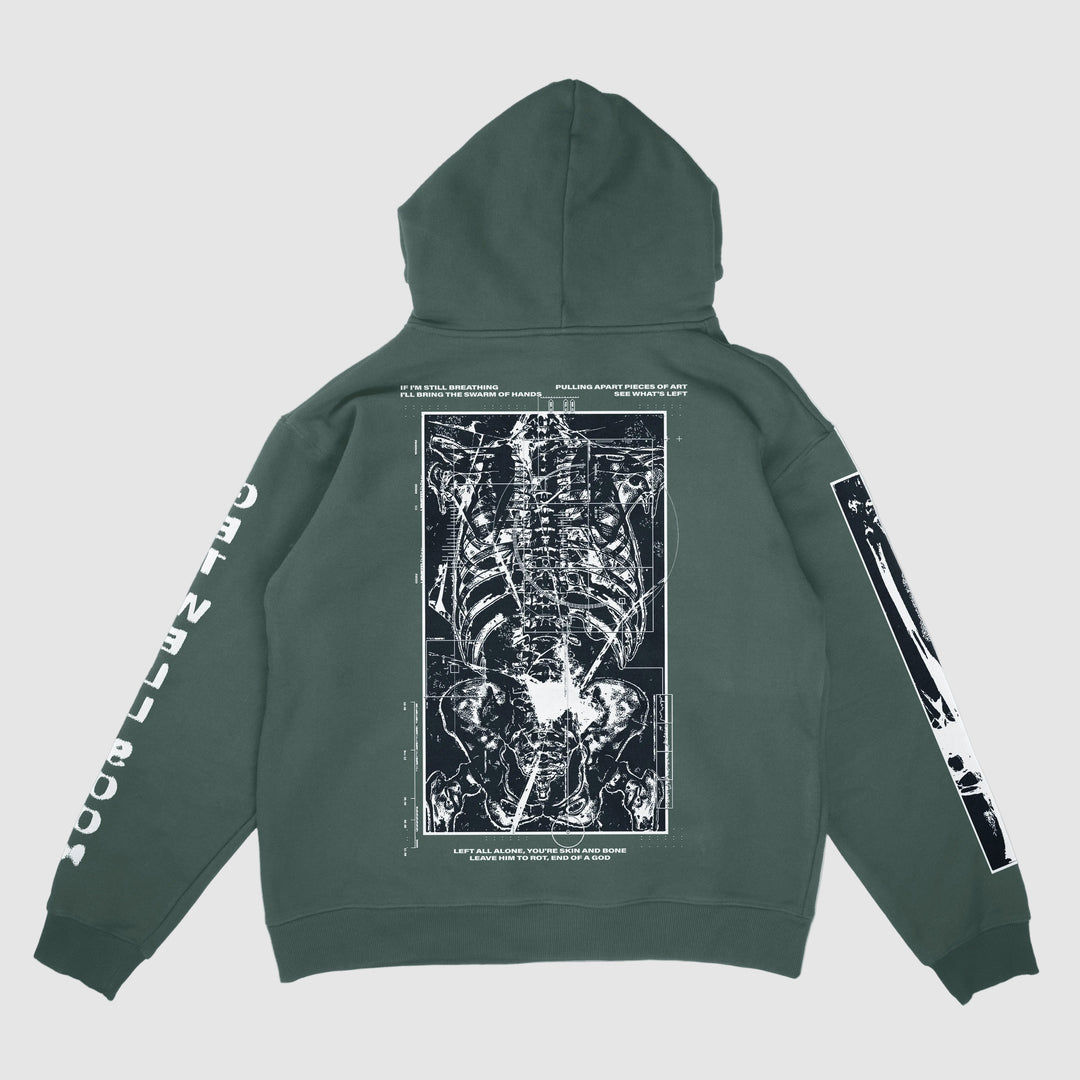 A Johnny Booth forest green Comfort Colors hoodie with a bold white anatomical X-ray skeleton print on the back, surrounded by white text and diagrams, plus matching garment graphics and text printed along both sleeves.