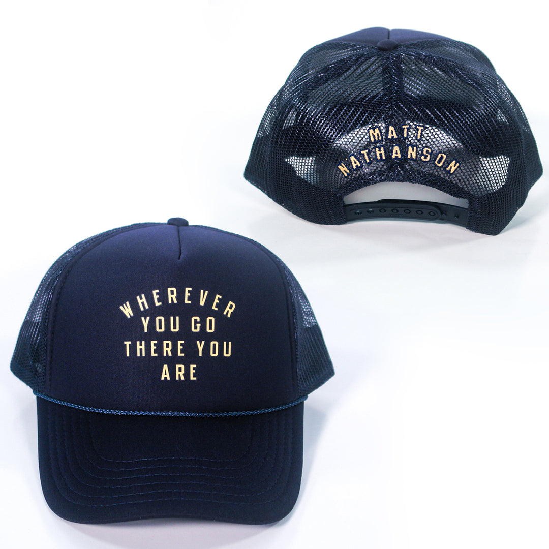 Two navy blue mesh Matt Nathanson Trucker Hats: one features WHEREVER YOU GO THERE YOU ARE in white on the front, while the back of the other displays MATT NATHANSON above the adjustable strap.