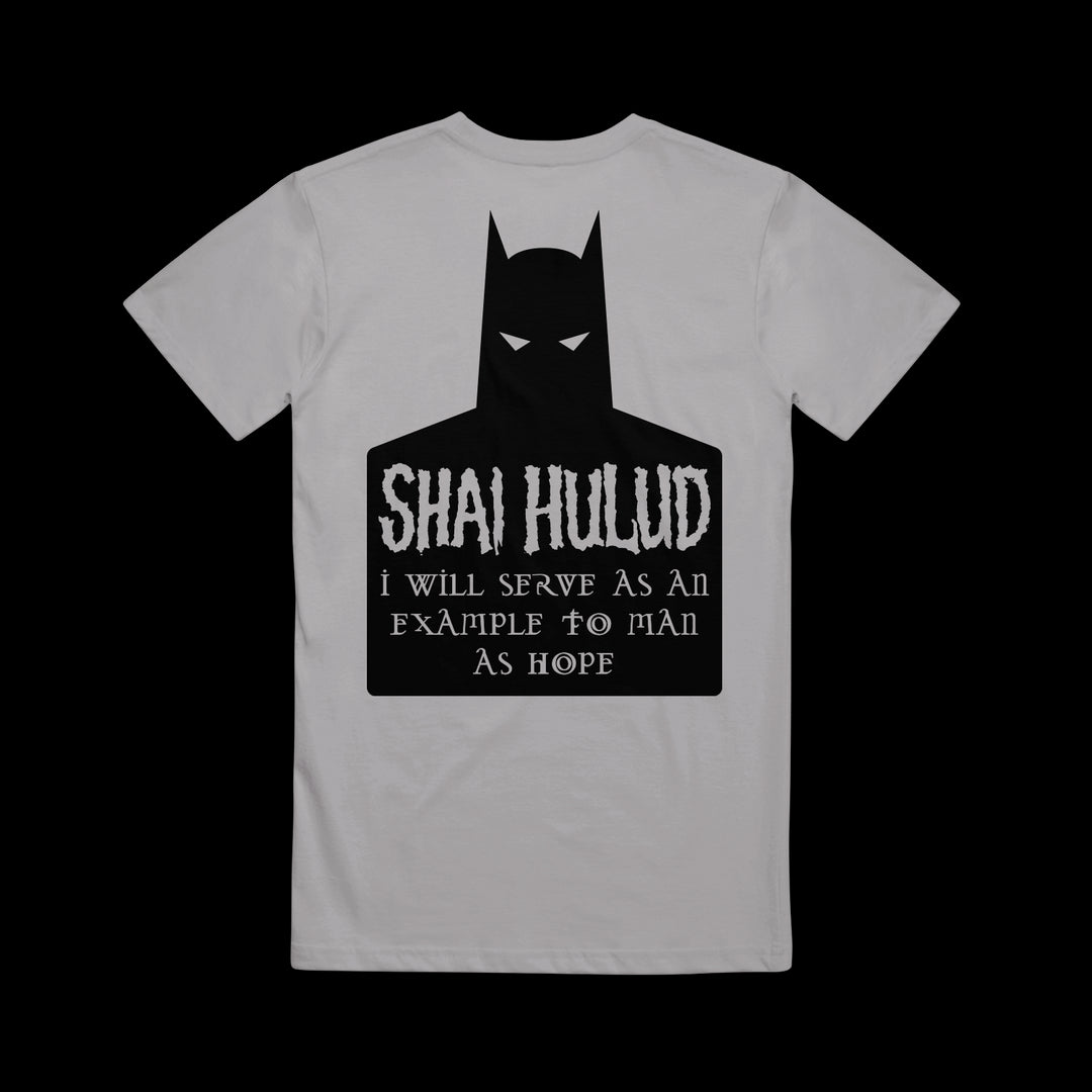 A gray Shai Hulud T-shirt features a black Batman silhouette with white eyes and the text: SHIA HULUD I will serve as an example to man as hope. The printed shirt is laid flat on a black background.