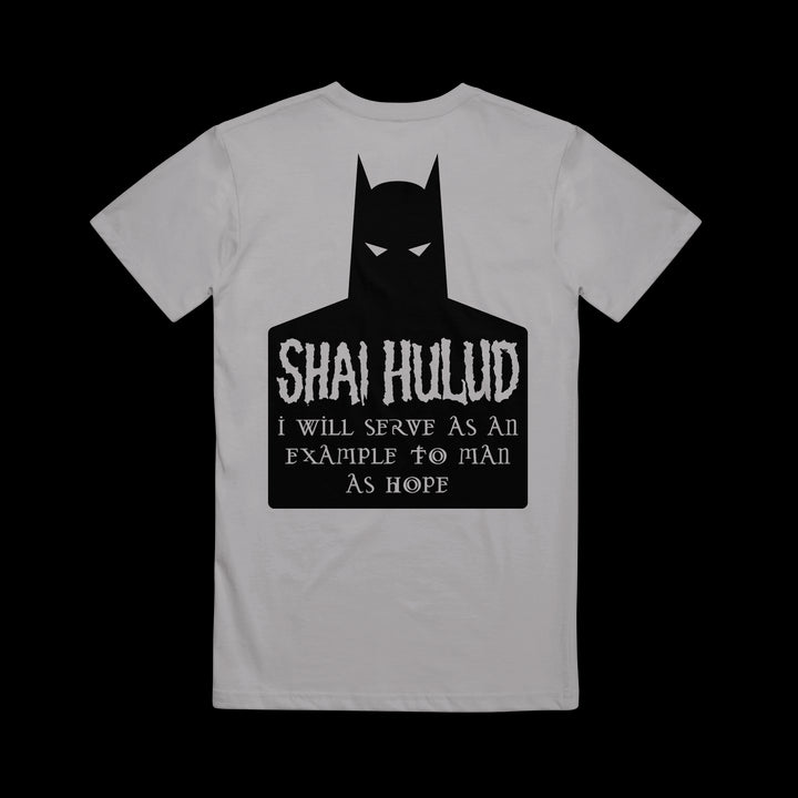 A gray Shai Hulud T-shirt features a black Batman silhouette with white eyes and the text: SHIA HULUD I will serve as an example to man as hope. The printed shirt is laid flat on a black background.
