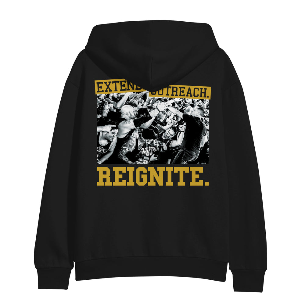 This Shai Hulud black Gildan Heavy Blend pullover hoodie displays a printed black and white concert crowd photo with people cheering. Yellow text above reads EXTENDED OUTREACH; below, bold yellow letters spell REIGNITE.