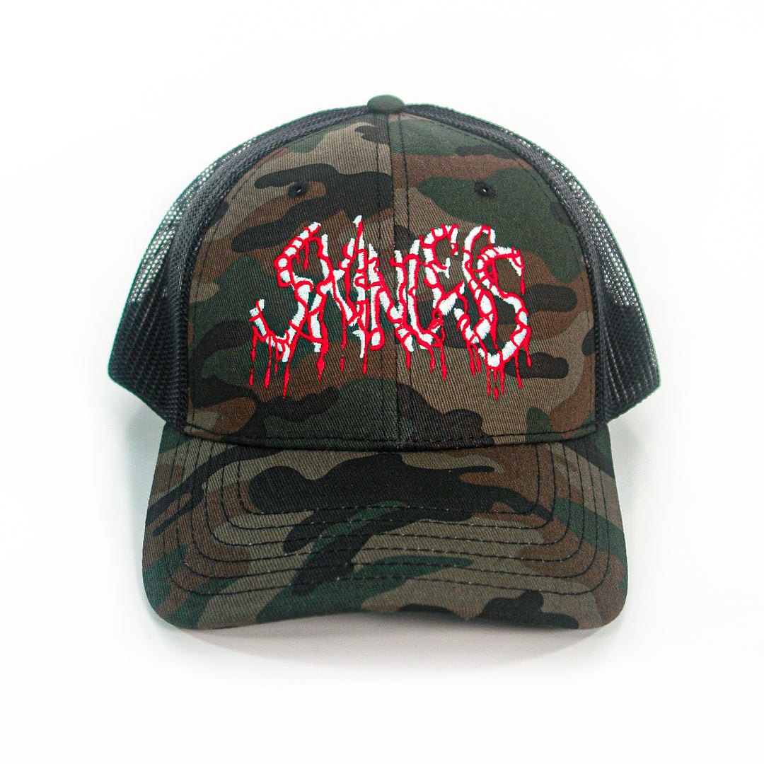 The Skinless camo trucker hat features a mesh snapback design and "SNACKS" on the front in bold white and red dripping font, resembling blood.