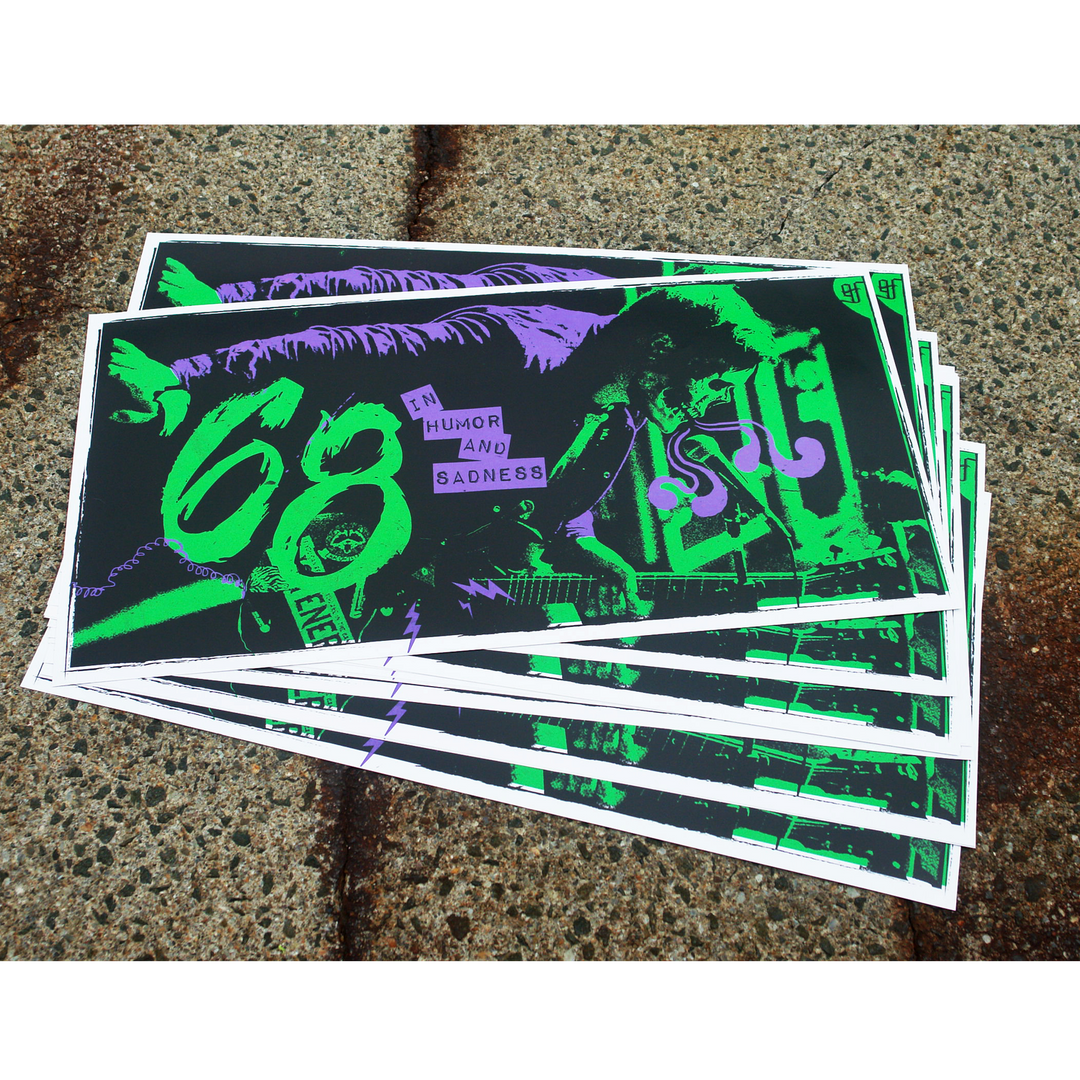 A stack of glossy '68 posters with a green and purple design and the text “IN HUMOR AND SADNESS” displayed on a textured concrete surface.